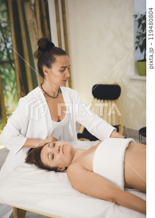 Beautiful female chiropractor works with woman who lying face up on massage table in pro salon, vertical image, selective focus. Beautiful female chiropractor works with woman who lying face up on massage table in pro salon, vertical image, selective focus. 119480804