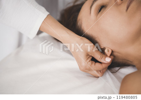 Therapists hand massage female earlobe, close-up. Woman lying on back on massage table, selective focus. Therapists hand massage female earlobe, close-up. Woman lying on back on massage table, selective focus. 119480805