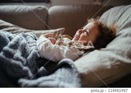 Sick girl with fever and cold lying on sofa under blanket, feeling tired. Sick girl with fever and cold lying on sofa under blanket, feeling tired. 119481497