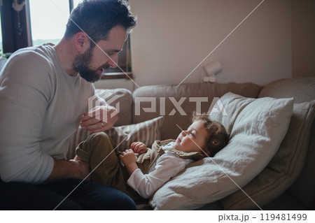 Father taking care of sick girl with fever and cold at home. Daughter lying on sofa, feeling tired. Father taking care of sick girl with fever and cold at home. Daughter lying on sofa, feeling tired. 119481499