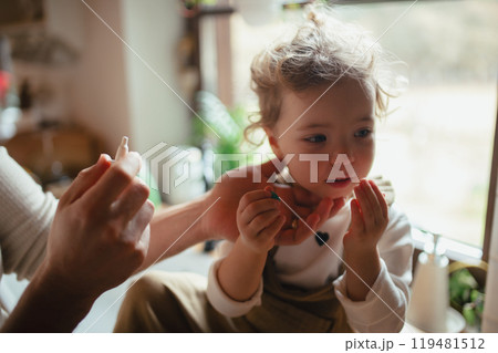Sick girl with cold at home has stuffy nose. Father helping little daughter to breath better, using nasal spray in his nose. 119481512