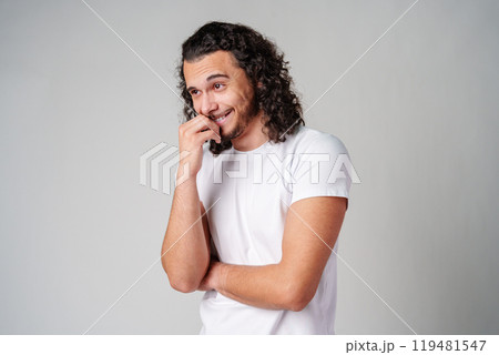 A young man stands thoughtfully against a plain background, expressing contemplation 119481547