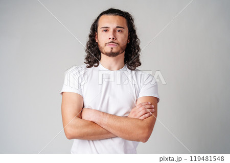 A young man stands thoughtfully against a plain background, expressing contemplation 119481548