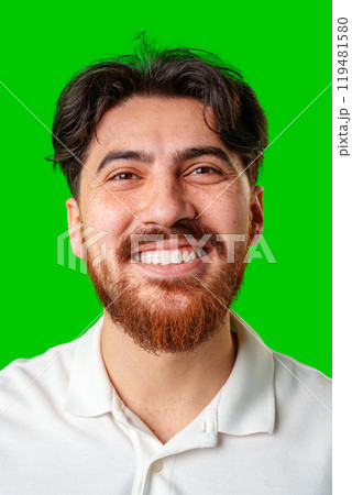 A smiling young man with a beard poses against a bright green background A smiling young man with a beard poses against a bright green background 119481580