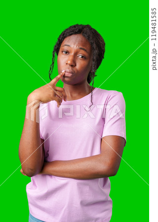 Thoughtful woman pondering in front of a bright green background during a casual moment Thoughtful woman pondering in front of a bright green background during a casual moment 119481585