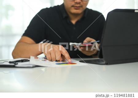Young creative man working on a design project reviewing color chart and using laptop at desk 119481881