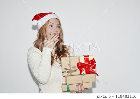 Surprised Woman Holding Christmas Gifts Wearing Santa Hat 119482110