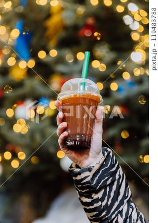 Festive takeaway drink held up against glowing Christmas lights, perfect for cold holiday evenings Festive takeaway drink held up against glowing Christmas lights, perfect for cold holiday evenings 119483788