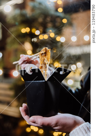 Steaming Asian noodles in a takeaway box under festive city lights, perfect for an evening snack 119483790