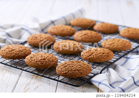 Freshly baked oatmeal cookies cooling on a black wire rack, with in a light kitchen table, selective focus. Freshly baked oatmeal cookies cooling on a black wire rack, with in a light kitchen table, selective focus. 119484214
