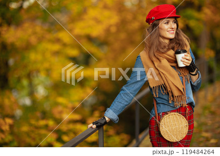 smiling young woman in jeans shirt and red hat with scarf 119484264
