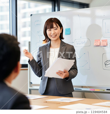 会議室でボードを前に資料を笑顔で説明するスーツ姿の女性2 119484584