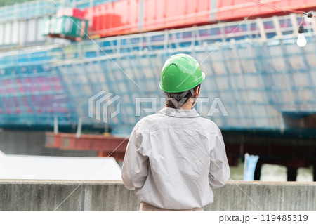 建設中の橋を見つめるヘルメットを被った作業服姿の女性 119485319