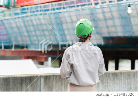 建設中の橋を見つめるヘルメットを被った作業服姿の女性 119485320