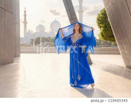 Travel to the United Arab Emirates, Abu Dhabi. Woman in blue Arabic dress near Sheikh Zayed Great white mosque. famous Abu Dhabi sightseeing. Travel to the United Arab Emirates, Abu Dhabi. Woman in blue Arabic dress near Sheikh Zayed Great white mosque. famous Abu Dhabi sightseeing. 119485345