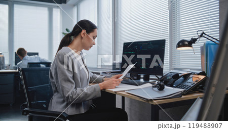 Adult, beautiful female analyst checking data in paper documents Adult, beautiful female analyst checking data in paper documents 119488907