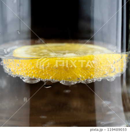 A bright yellow lemon slice rests on the surface of sparkling water, with bubbles forming around it 119489033
