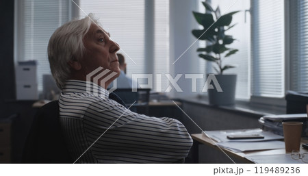 Tired senior financial specialist analyzes documents, monitors stock market on computer 119489236