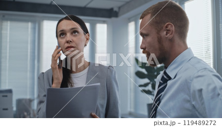 Female financial specialist talks to business client using phone, male colleague stands near 119489272