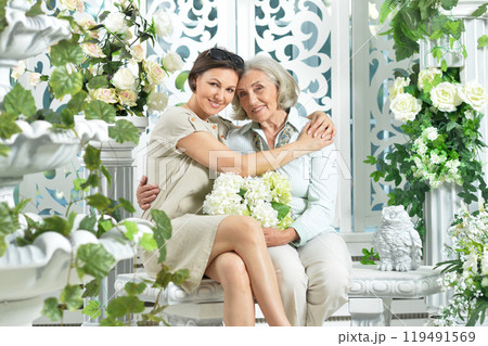 Elderly mother and daughter sitting on a bench surrounded by flowers 119491569