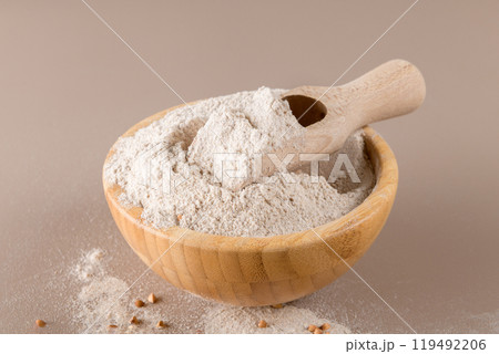 Buckwheat flour in a wooden bowl with wooden scoop on beige background Buckwheat flour in a wooden bowl with wooden scoop on beige background 119492206