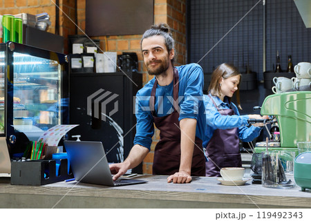 Two cafe workers working together behind counter, at coffee shop Two cafe workers working together behind counter, at coffee shop 119492343