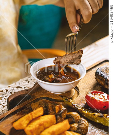 Person dipping grilled meat in sauce with fork Person dipping grilled meat in sauce with fork 119492469