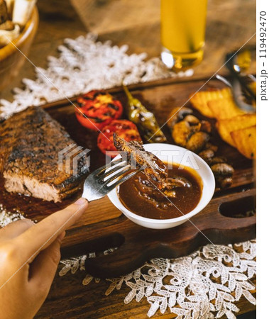 Person dipping grilled steak in sauce with beer in background Person dipping grilled steak in sauce with beer in background 119492470