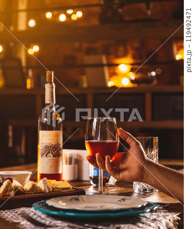 Person holding glass of wine with cheese and wine bottle on table Person holding glass of wine with cheese and wine bottle on table 119492471