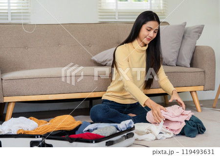 Young Woman Folding Clothes and Packing Them into a Suitcase in a Modern Living Room for Travel or Vacation Preparation Young Woman Folding Clothes and Packing Them into a Suitcase in a Modern Living Room for Travel or Vacation Preparation 119493631