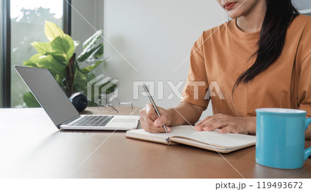 Young Girl Studying Online from Home with Laptop and Notebook, Engaged in E-Learning in a Modern Home Environment 119493672