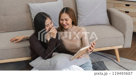 Happy Lesbian Couple Relaxing in Modern Living Room, Reading and Laughing Together on Comfortable Sofa 119493687