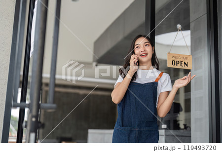 Young Barista Preparing for the Opening of the Coffee Shop with a Smile and a Phone Call Young Barista Preparing for the Opening of the Coffee Shop with a Smile and a Phone Call 119493720