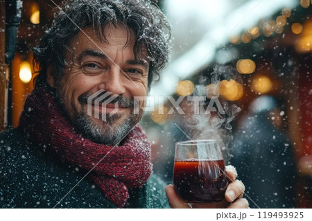 Close-up of a happy European man enjoying a warm drink at a festive winter market with snow and holiday lights 119493925