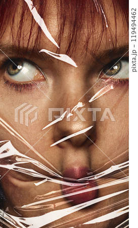 Close-up of female face wrapped in plastic cover. Woman making funny, grimacing face. Conceptual photography. 119494462