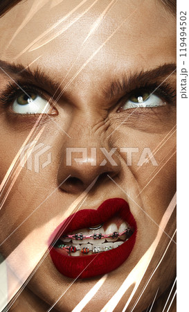 Close-up of female face with red lips makeup, braces, expressing emotions of annoyance and boredom. Conceptual photography. 119494502