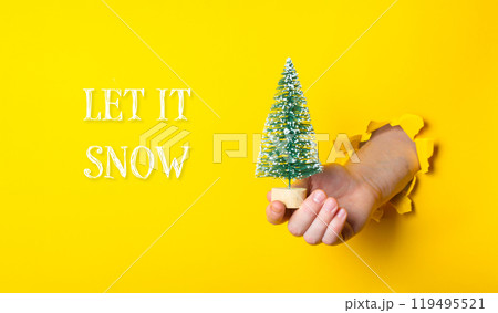 A hand holding a small Christmas tree in front of a yellow background 119495521