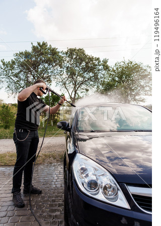 Man Using High-Pressure Washer to Clean a Black Car Under a Sunny Sky Man Using High-Pressure Washer to Clean a Black Car Under a Sunny Sky 119496164