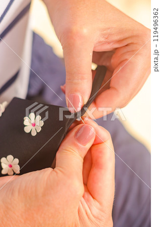 hands of a senior woman who uses needle and thread to repair a black garment. . High quality photo 119496362