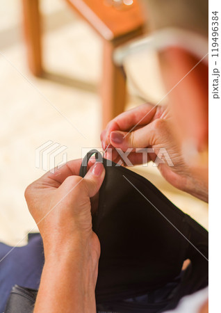 The hands of a senior woman who uses needle and thread to repair a black garment. High quality photo 119496384