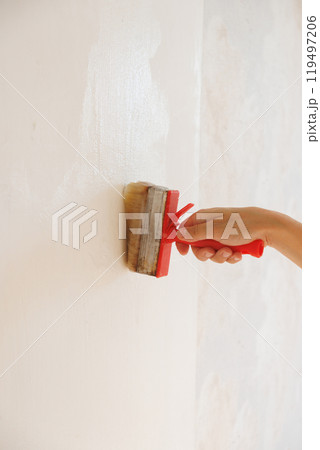Person is holding brush with glue on background of light wall. apply thick wallpaper glue. Person is holding brush with glue on background of light wall. apply thick wallpaper glue. 119497206