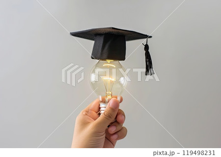 An individual is holding a light bulb that is wearing a graduation cap 119498231