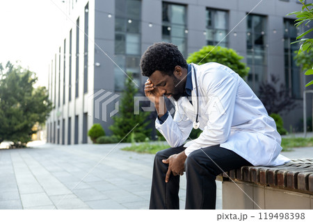 Stressed tired medical practitioner man sitting outside near clinic 119498398