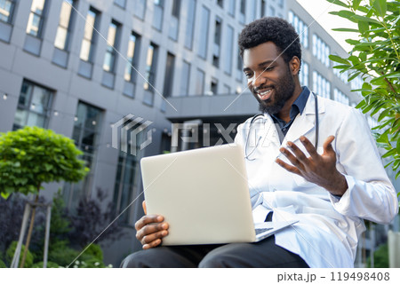 Bearded doctor wearing his uniform at hospital using his laptop to research medical data 119498408