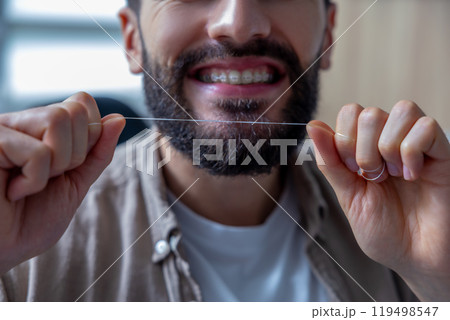 Man holding dental floss following hygiene routine to maintain fresh and healthy teeth and braces 119498547