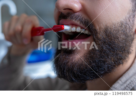 Man with beard in dental clinic holding toothbrush while cleaning teeth maintaining oral hygiene 119498575