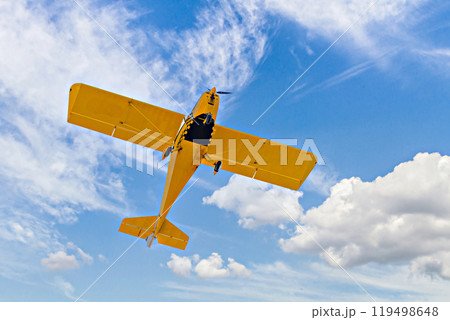 Yellow single-engine ultralight airplane flying in the blue sky with white clouds Yellow single-engine ultralight airplane flying in the blue sky with white clouds 119498648