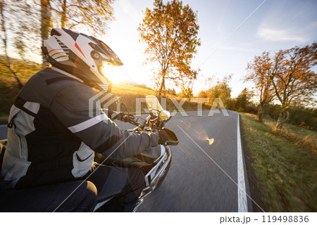 Driver riding motorcycle on empty road during sunset, handlebar view, autumn mountains 119498836
