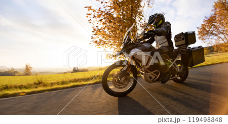 Driver riding motorcycle on empty road during sunset, autumn mountains 119498848