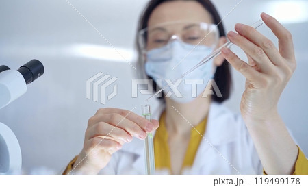 Woman with safety glasses and blue mask is working with lab tubes using a pipette in a modern laboratory, close-up of researcher. Science and medicine 119499178